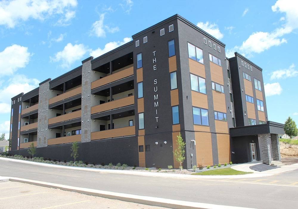 the-summit-seniors-apartment-brandon-smaller Exterior of The Summit apartment building on Braecrest Drive in Brandon, Manitoba as viewed from the southwest. The three-storey building is painted dark grey with brown accents.